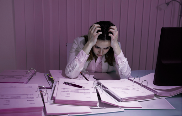 A frustrated healthcare professional surrounded by paperwork, highlighting the burden of manual temperature checks and outdated monitoring systems